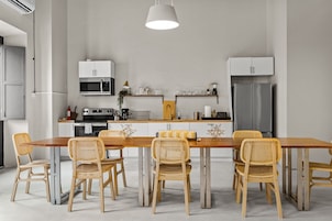 A modern kitchen with a wooden dining table and chairs, a built-in oven, and a refrigerator.