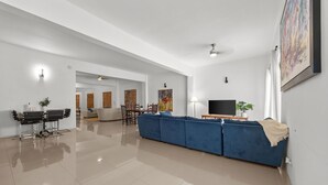 A spacious living area with a blue sofa, a dining table with chairs, and a television.