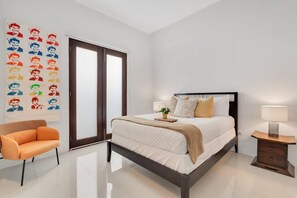 Quarto com cama, uma cadeira, mesa de cabeceira e uma parede decorada com obras de arte.