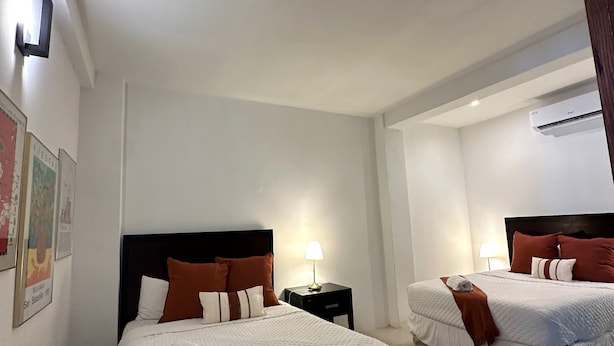 A hotel room with two beds, a nightstand with a lamp, and an air conditioning unit on the wall.