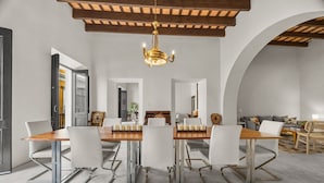 A dining area with a long wooden table, white chairs, and a chandelier.