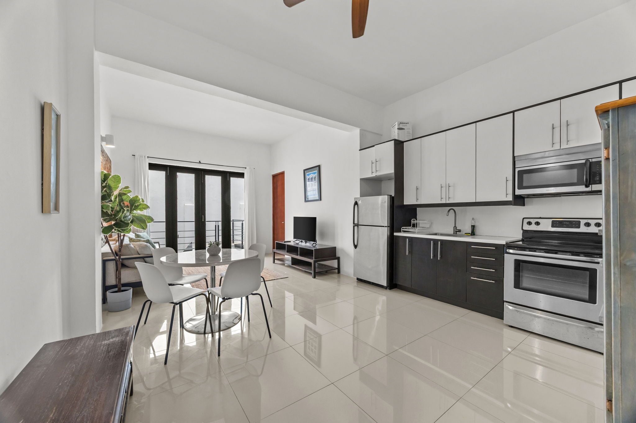A modern kitchen with stainless steel appliances, a dining area with a round table and chairs, and a large window providing natural light.