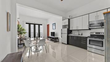 A modern kitchen with stainless steel appliances, a dining area with a round table and chairs, and a large window providing natural light.