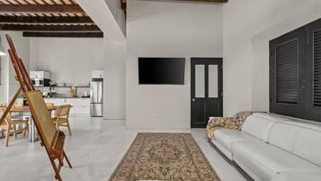 A modern living room with a white sofa, a patterned rug, a painting easel, and a flat-screen TV mounted on the wall.