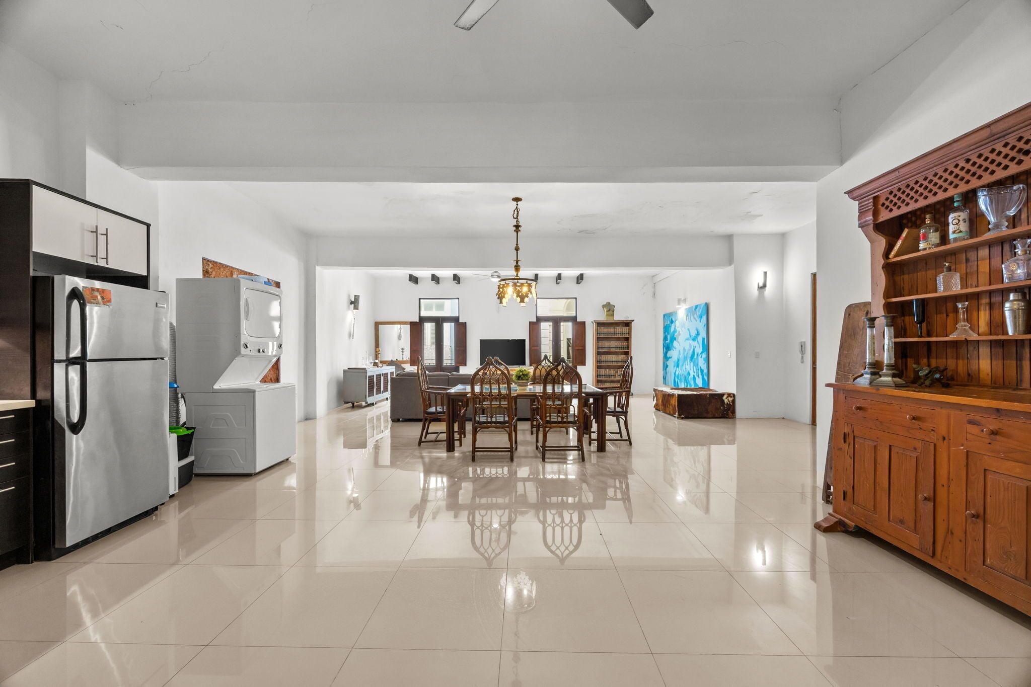 A spacious kitchen with modern appliances, a dining area with a chandelier, and a wooden cabinet with glassware.