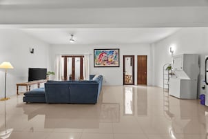 A spacious living area with a blue sofa, a flat-screen TV, and a ceiling fan.