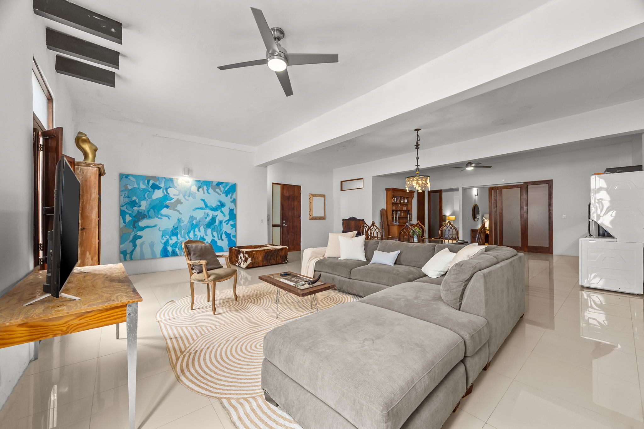 A spacious living room with a large grey sectional sofa, a wooden coffee table, and a modern ceiling fan.