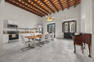 Una cocina amplia con electrodomésticos modernos, un comedor con mesa y sillas de madera, y un piano en la esquina.
