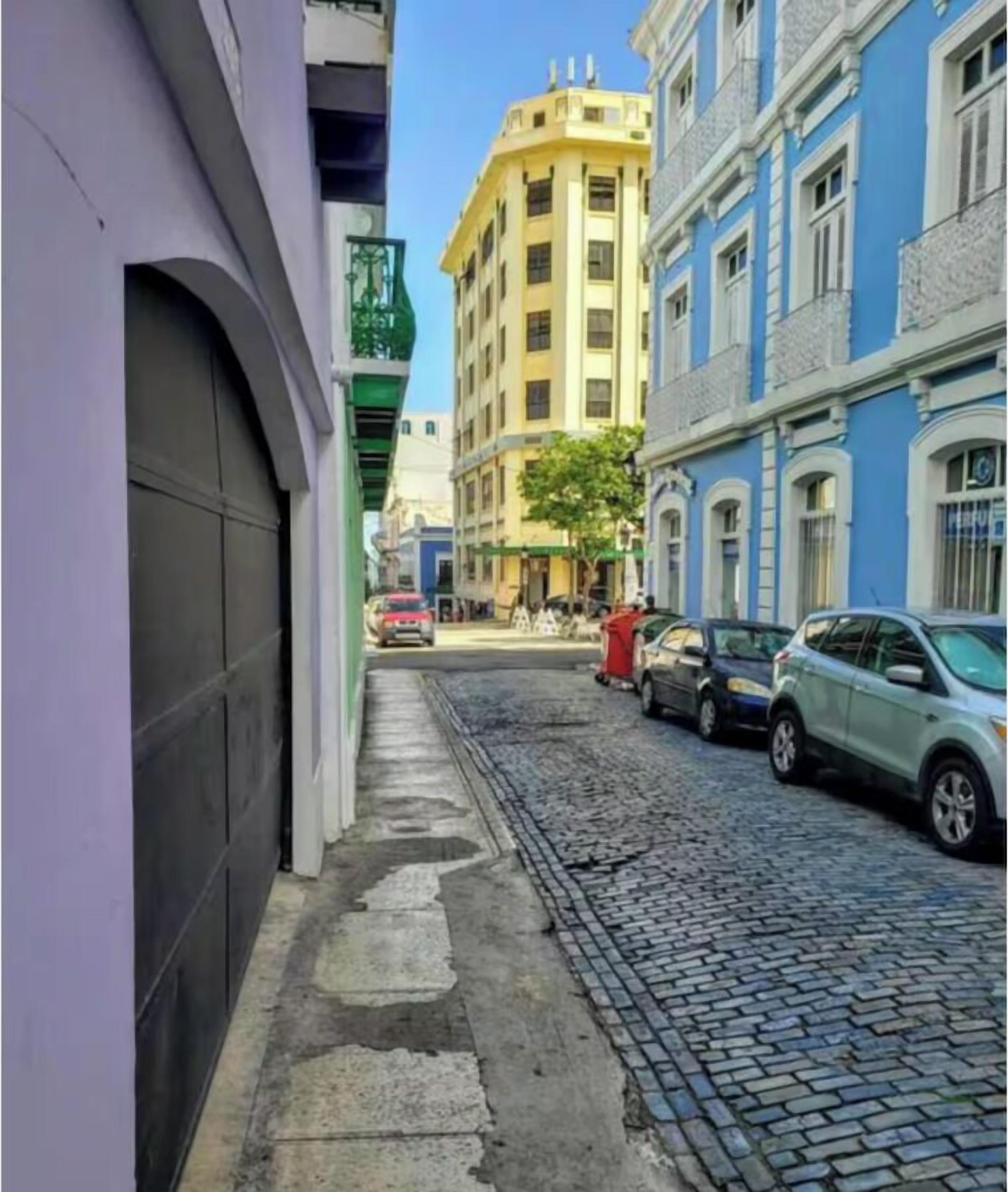 Una estrecha calle adoquinada flanqueada por edificios, incluyendo un edificio de esquina amarillo y uno azul con detalles blancos.