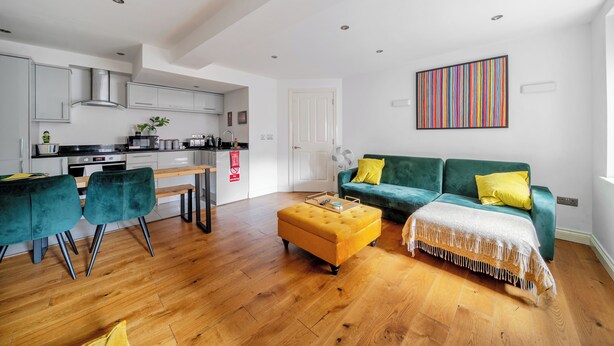 A modern living space with a kitchen, a green sofa, and a wooden dining table. - Lace Market - 1-bed Apt - Sleeps 3 - City Centre (Nottingham)