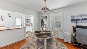 Un coin repas avec une table ronde, des chaises, un lustre et une vue sur la cuisine.