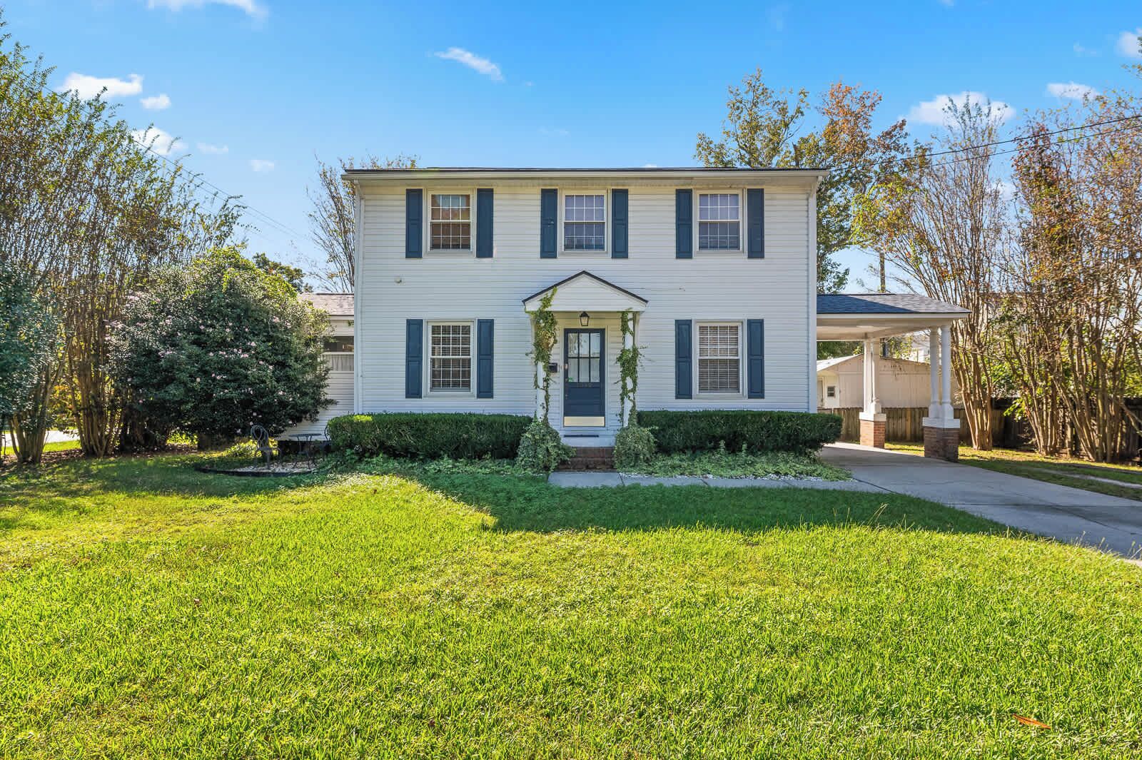 A two-story house with a front porch, a small garden, and a clear blue sky.