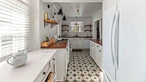 Une cuisine avec des meubles blancs, un carrelage noir et blanc et un réfrigérateur blanc.