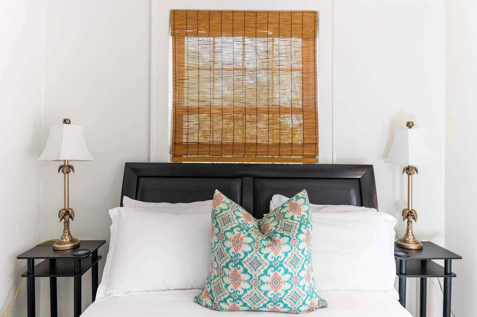 A neatly made bed with white linens, a patterned pillow, and two bedside lamps on black nightstands.