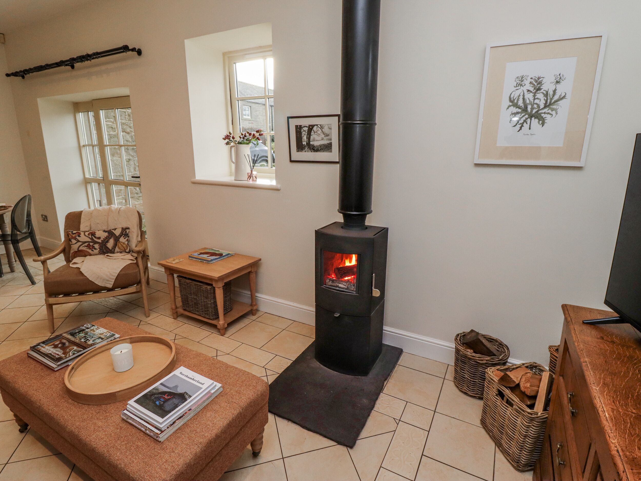 A cozy living room with a black wood-burning stove, a comfortable armchair, a small table with magazines, and a wicker basket.