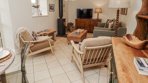 A cozy living room with a fireplace, comfortable seating, a television, and a wooden cabinet. - Watermill Cottage (Chathill)