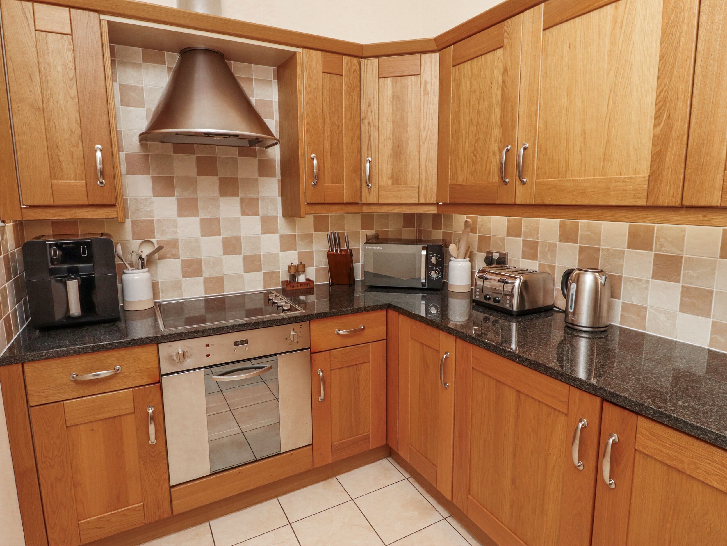 A modern kitchen with wooden cabinets, a built-in oven, a coffee maker, a toaster, and a kettle.