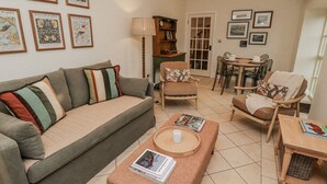 A cozy living room with a sofa, armchairs, a coffee table, and a dining area with chairs and a table. - Watermill Cottage (Chathill)
