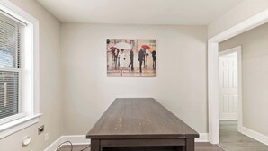 A room with a wooden table, a painting on the wall, and a door in the background. - Stylish North Charleston Stay | Comfort + Convenience (North Charleston)