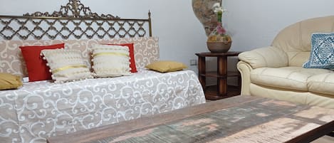 Una sala de estar con un sofá estampado, una mesa de centro de madera y una mesita auxiliar con un florero.