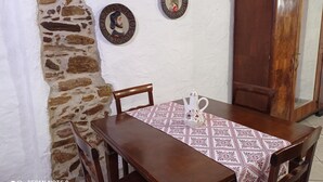 A dining area with a wooden table, chairs, a patterned tablecloth, and a teapot. There are two wall-mounted decorative plates and a wooden cabinet.