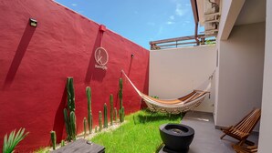 A red wall with a logo, a hammock, cacti, and wooden chairs in a courtyard.