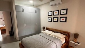 A bedroom with a wooden bed, a grey wardrobe, a ceiling fan, and framed pictures on the wall.