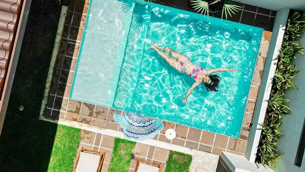A rooftop swimming pool with a person swimming, surrounded by potted plants and a stone wall.
