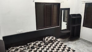 A bedroom with a bed, a window, a mirror, and a black shelf. - MANGAL DHAM DEOGHAR  (Deoghar)