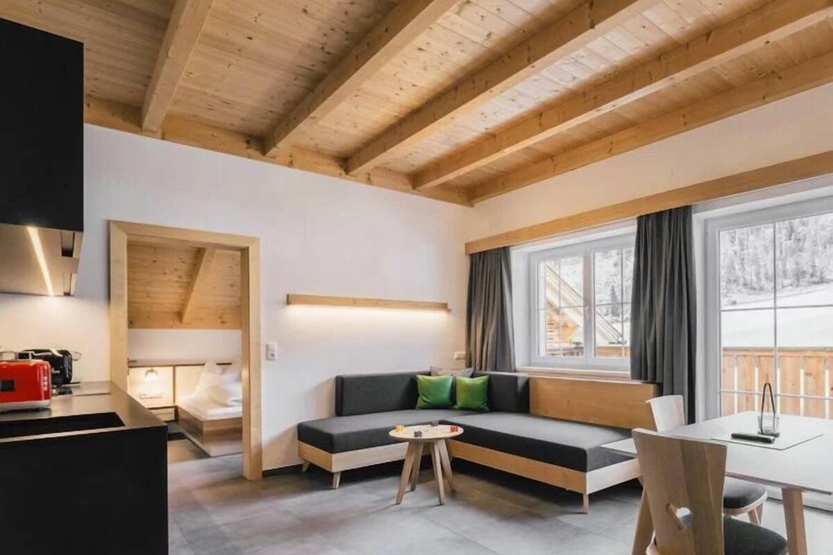 A modern interior with a wooden ceiling, a sofa, a dining table, and a kitchen area.