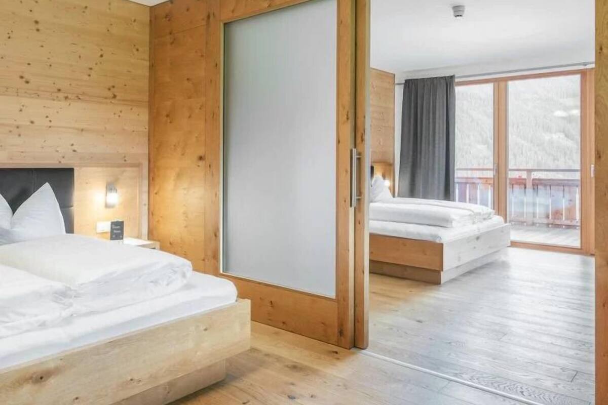 A wooden room with a bed and a sliding door leading to another room with a bed.