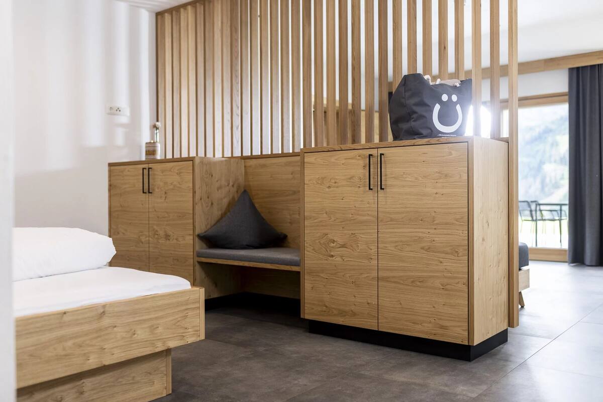 A modern bedroom with a wooden bed, a built-in bench, and a wardrobe with a large bag on top.