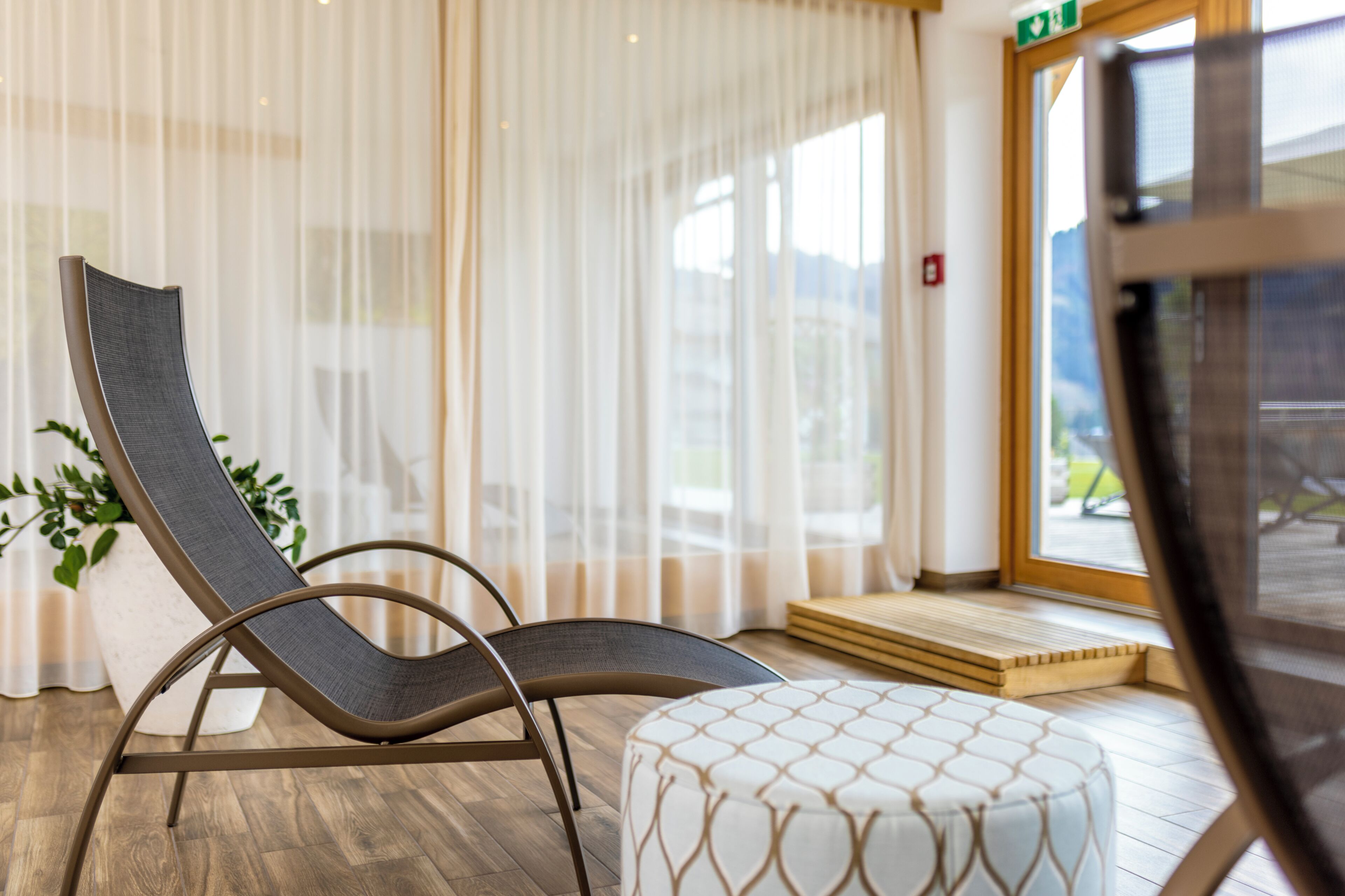 Ein Zimmer mit einem gepolsterten Sessel, einer Zimmerpflanze und Blick durch ein Fenster.