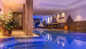 An indoor swimming pool with a clear water surface, lounge chairs, and a wooden wall. - Tillga Glück (Obertilliach)