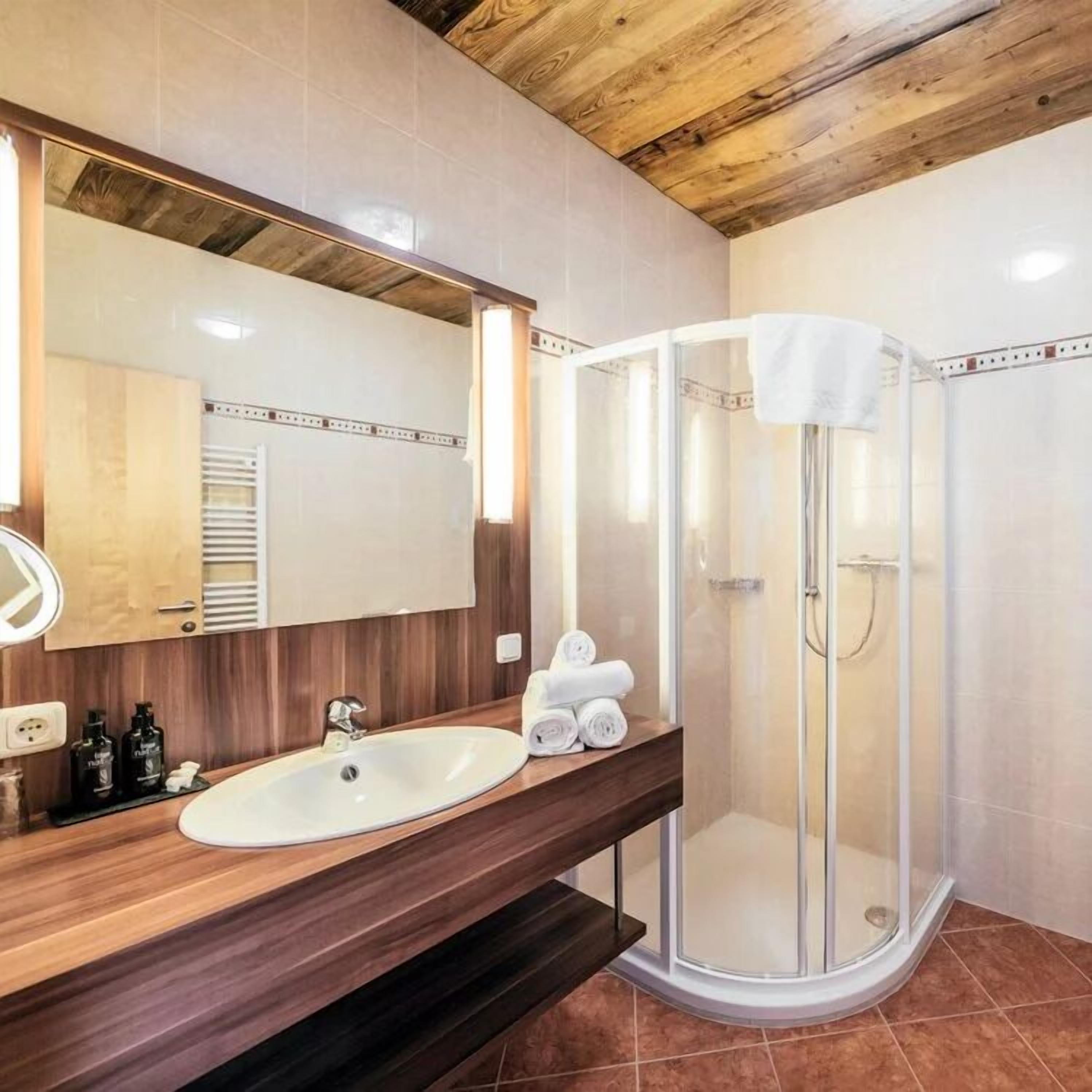 A bathroom with a wooden ceiling, a white sink, a mirror, and a glass shower enclosure.