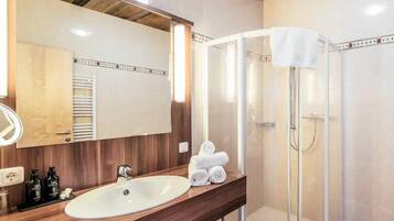 A bathroom with a wooden ceiling, a white sink, a mirror, and a glass shower enclosure.