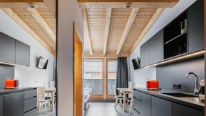 A modern kitchen with dark cabinetry, wooden beams, and a central island. - Tillga Glück (Obertilliach)