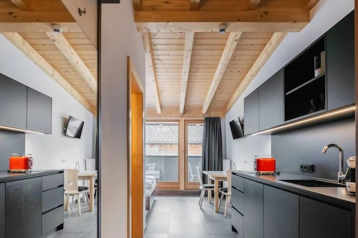 A modern kitchen with dark cabinetry, wooden beams, and a central island.