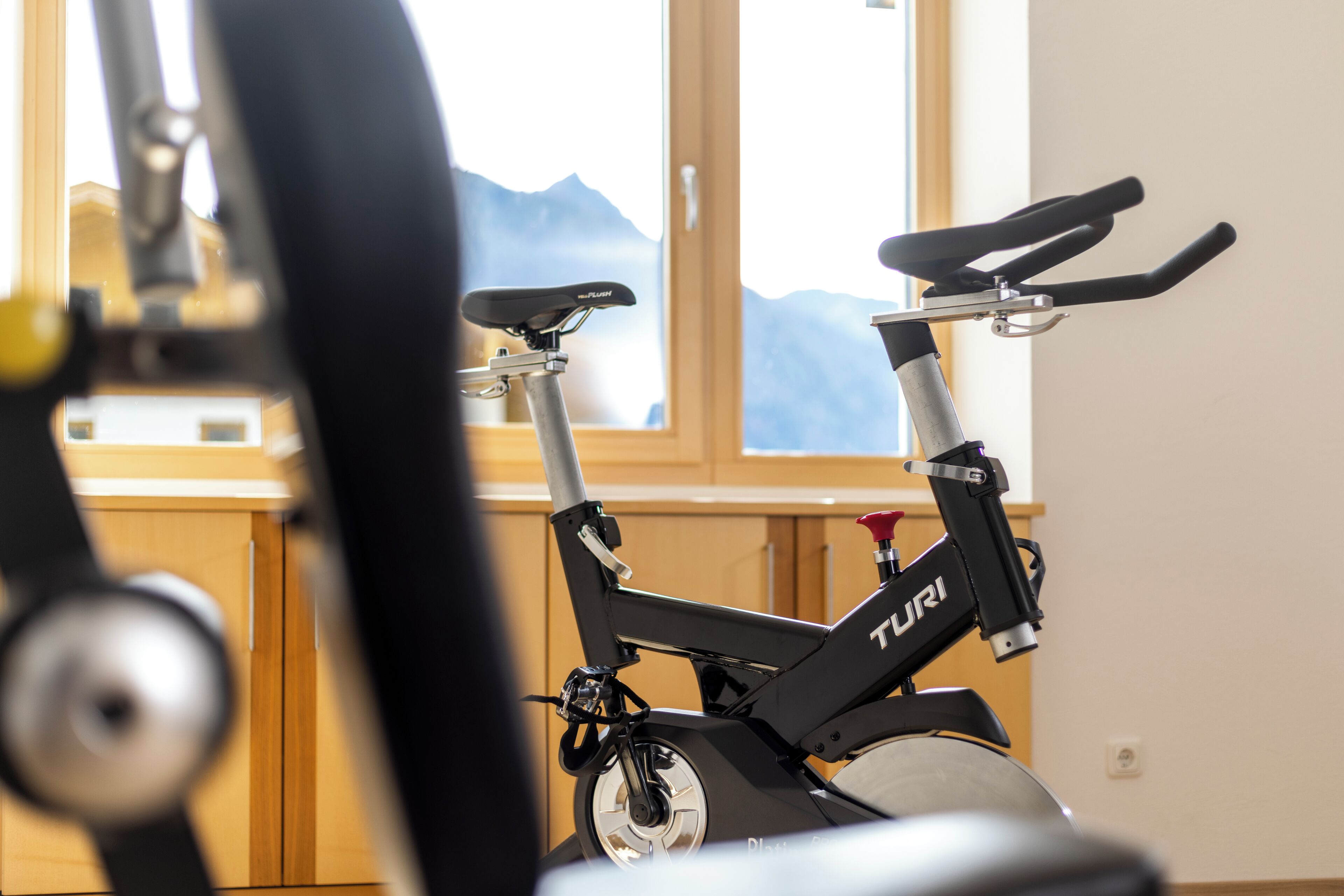 Una cyclette fissa con marchio 'TURI', collocata in una stanza con una finestra che si affaccia sulle montagne.