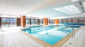 Ein großer, überdachter Pool mit Glaswänden, Holzsäulen und Blick auf verschneite Berge.