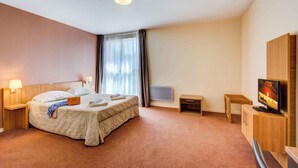 A hotel room with a bed, bedside lamps, a TV, a small table, and a cabinet. - Près des Pistes! Studio Charmant | Accès Sauna (La Féclaz)