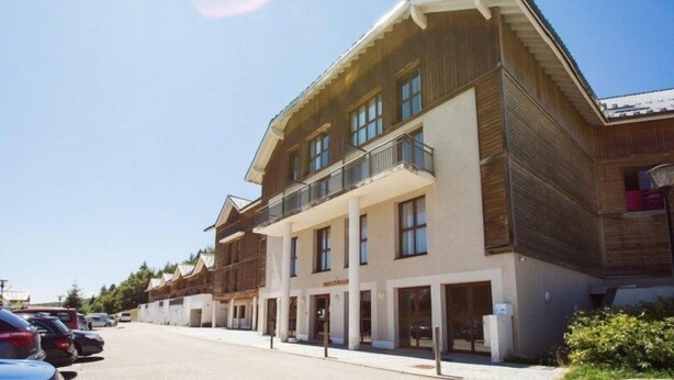 Een hotel met meerdere verdiepingen, een houten gevel, balkons en een parkeerplaats.