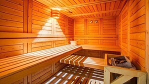 Een houten sauna met banken, een zitbank en een heater aan de wand, plus een klein tafeltje met een boek.