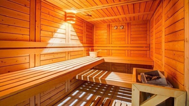 A wooden sauna with benches and a bench seat, a wall-mounted heater, and a small table with a book. - Près des Pistes! Studio Charmant | Accès Sauna (La Féclaz)