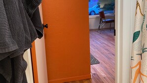 Un couloir avec une porte orange qui donne sur une pièce offrant une vue sur la rue.