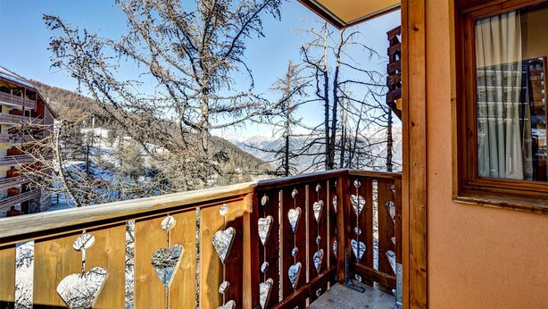 Un balcón de madera con recortes en forma de corazón y vistas de un paisaje montañoso.