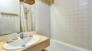 Un baño con lavamanos blanco, tocador de madera, espejo, ducha y paredes de azulejos.