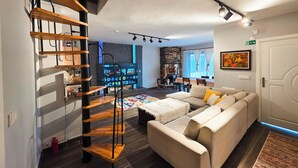 A modern living room with a wooden spiral staircase, a beige sofa, and a stone fireplace. - Villa Freya (Sapanca)