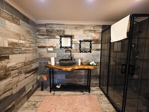 A bathroom with a rustic wooden wall, a wooden vanity with a sink, two mirrors, and a glass shower enclosure. - Villa Freya (Sapanca)