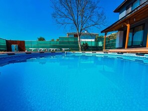 A clear blue swimming pool with lounge chairs, a wooden deck, and a building in the background. - Villa Freya (Sapanca)